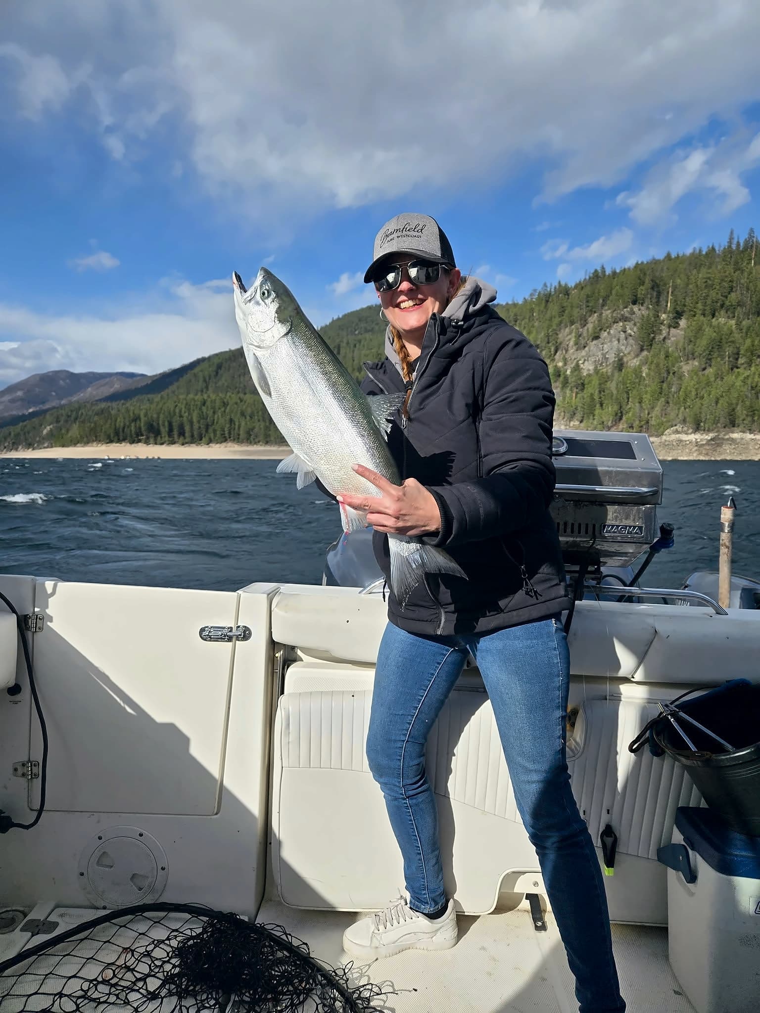 Tasha on a boat, smiling and holding up a big fish.