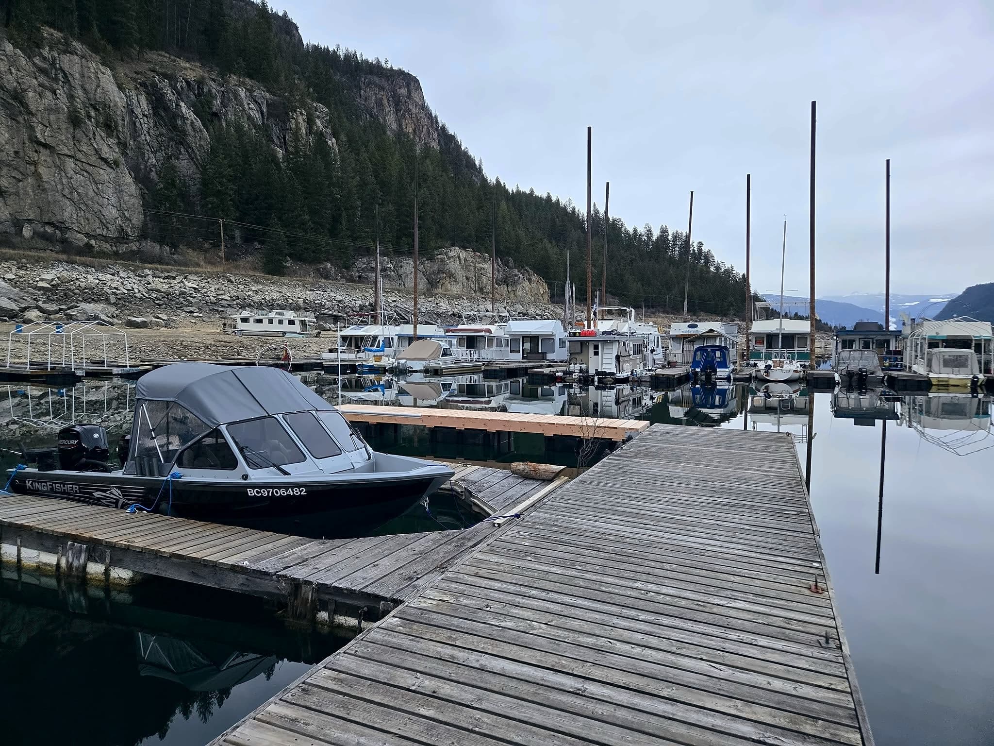 The walkway down the middle of the Scotties Marina docks, a covered boat tied alongside and the rock bluff behind.